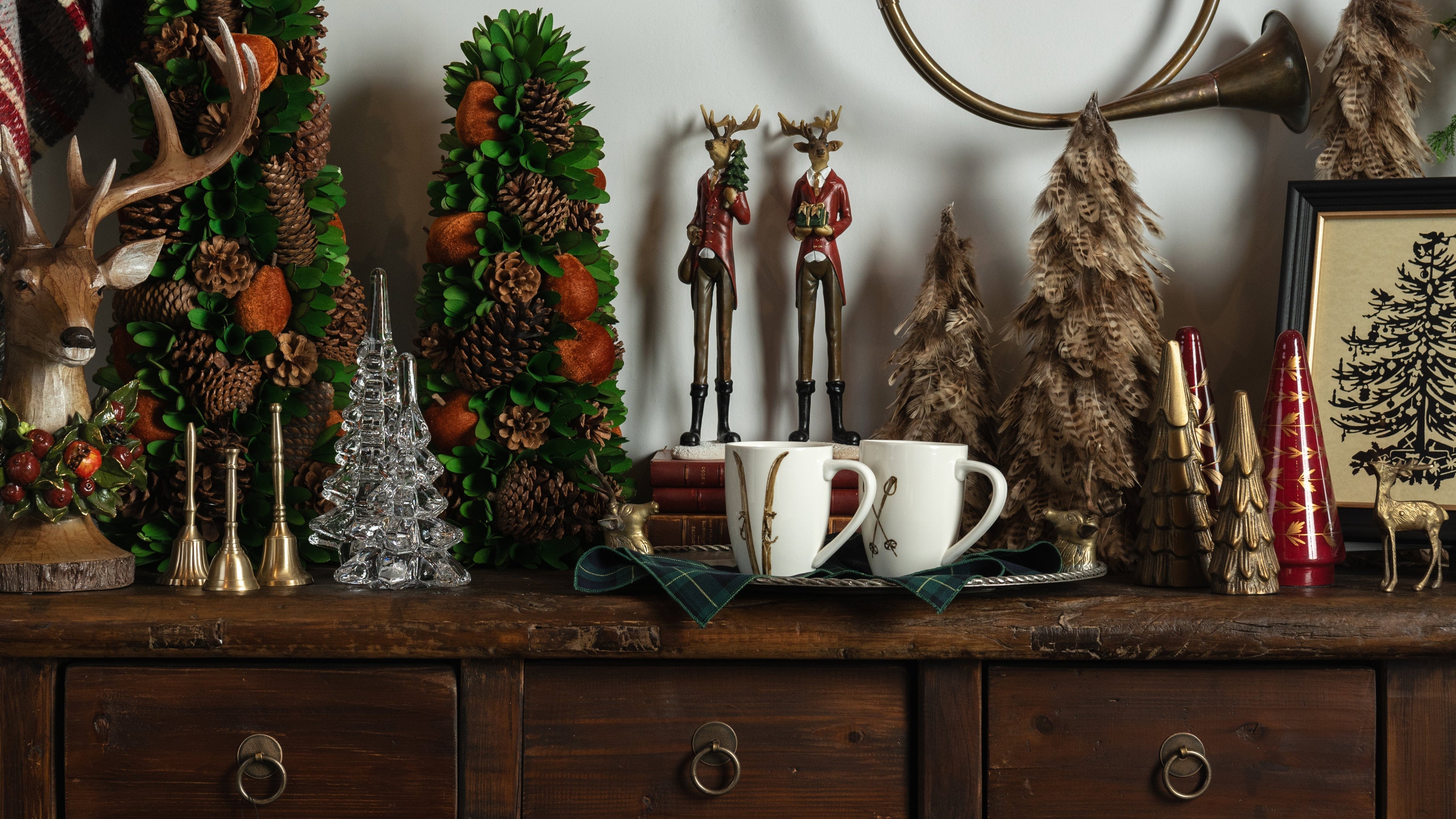 A tabletop styled with holiday decor, mugs, reindeer, trees, bells, artwork at Addison West