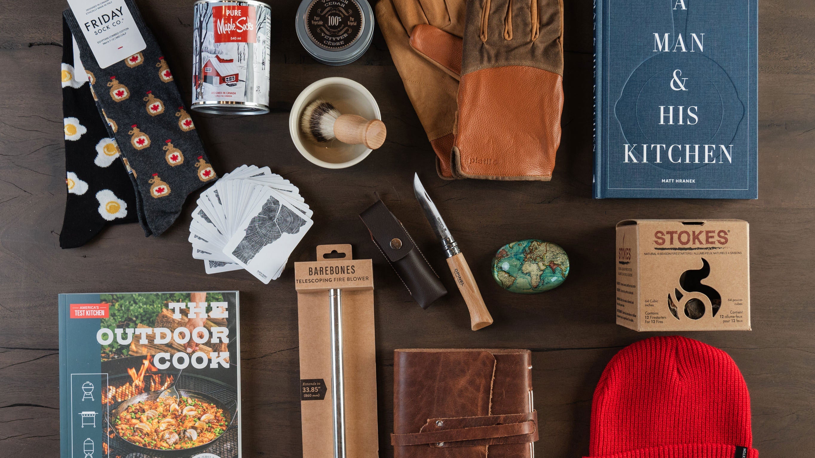 Gifts for men on a table including leather gloves, shaving kit, socks, hat, journal, books at Addison West