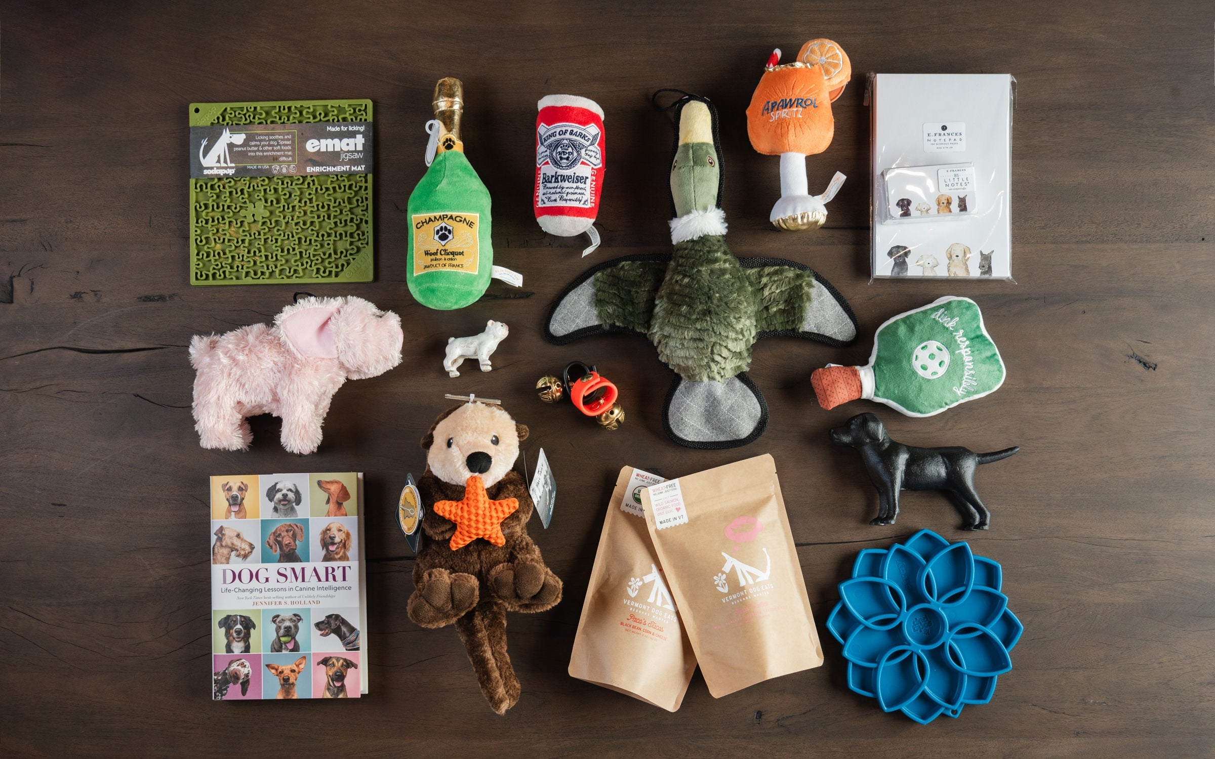 Collection of dog toys including lick mats, squeaky toys, dog books, and dog figurines on a dark wood table at Addison West