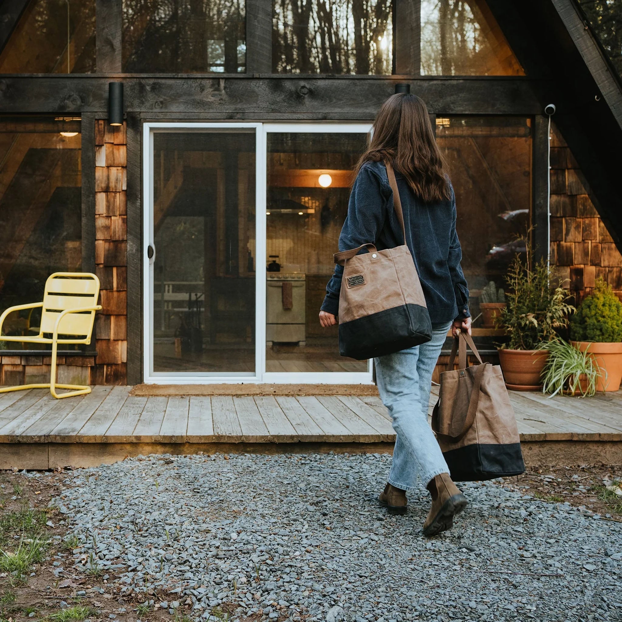 woman carrying two canvas grocery totes to a house at Addison West