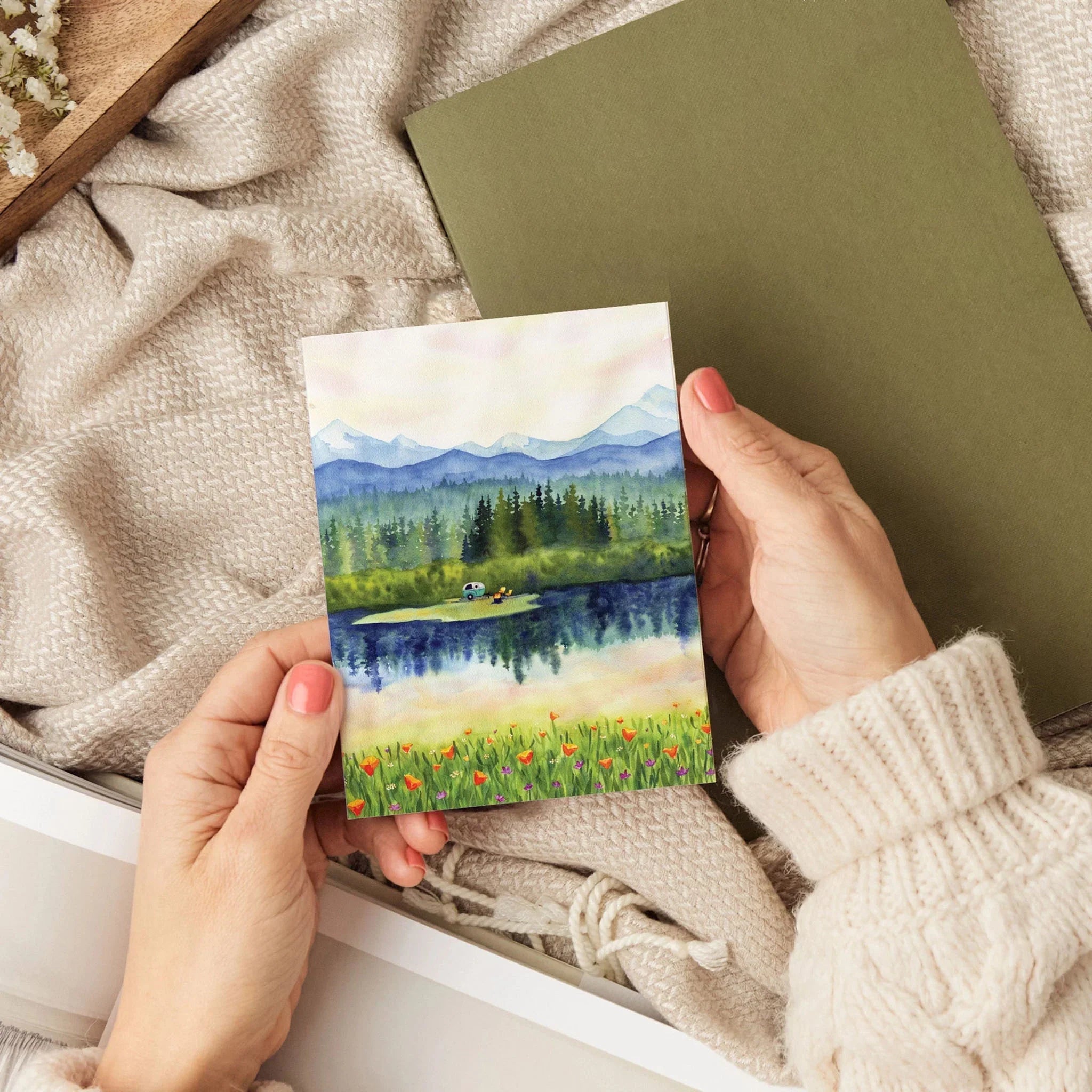 Photo of a watercolor handmade greeting card in someones hands against a blanket at Addison wEST