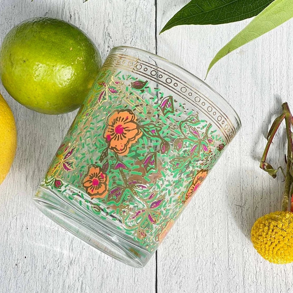 Drinking glass with green and organge floral pattern on a white wood surface