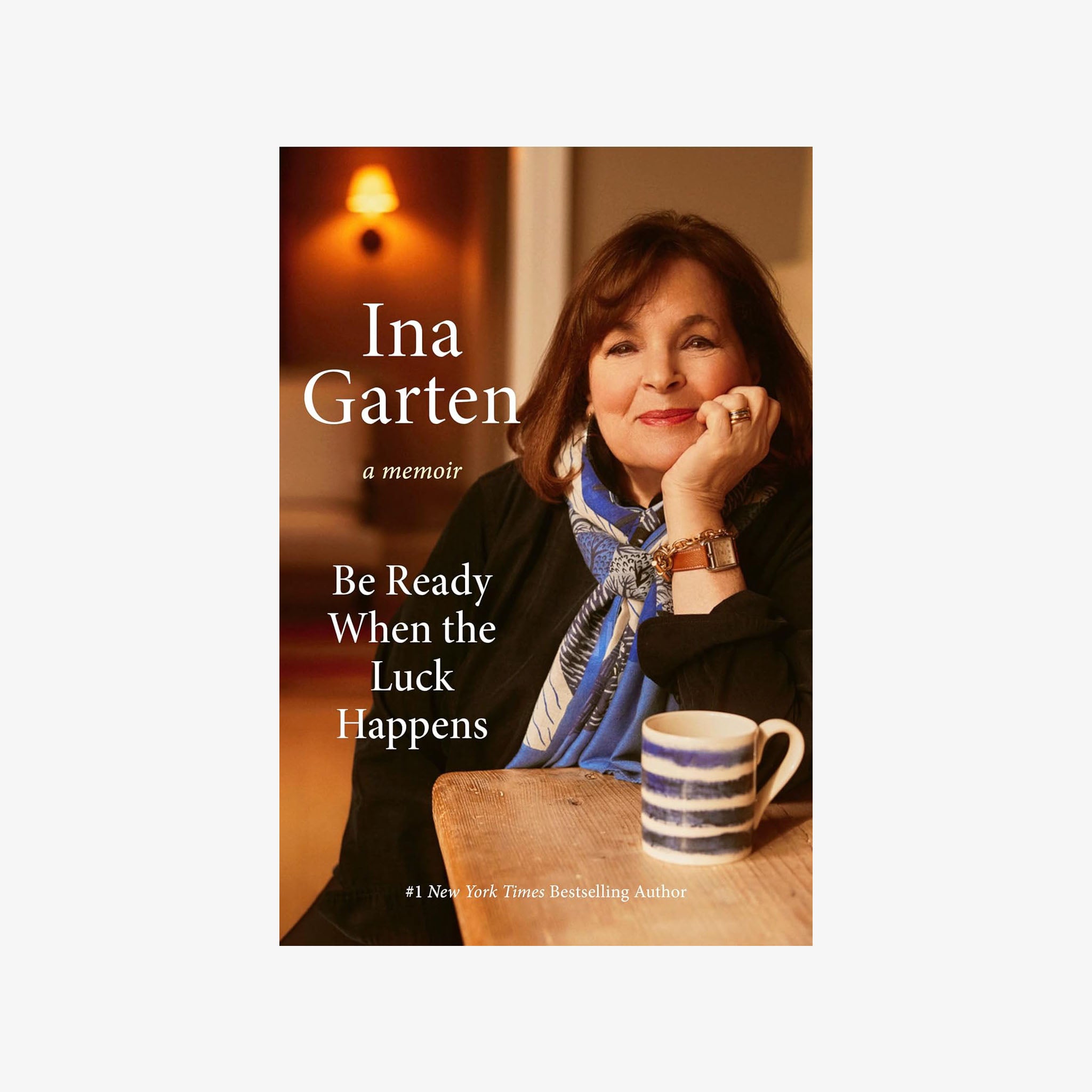 Front cover of book titled 'Be Ready When the Luck Happens'by Ina Garten with photo of the author on the front at a table with a striped coffee cup 