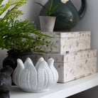 White marble lotus bowl on a shelf near decorative boxes and other items 