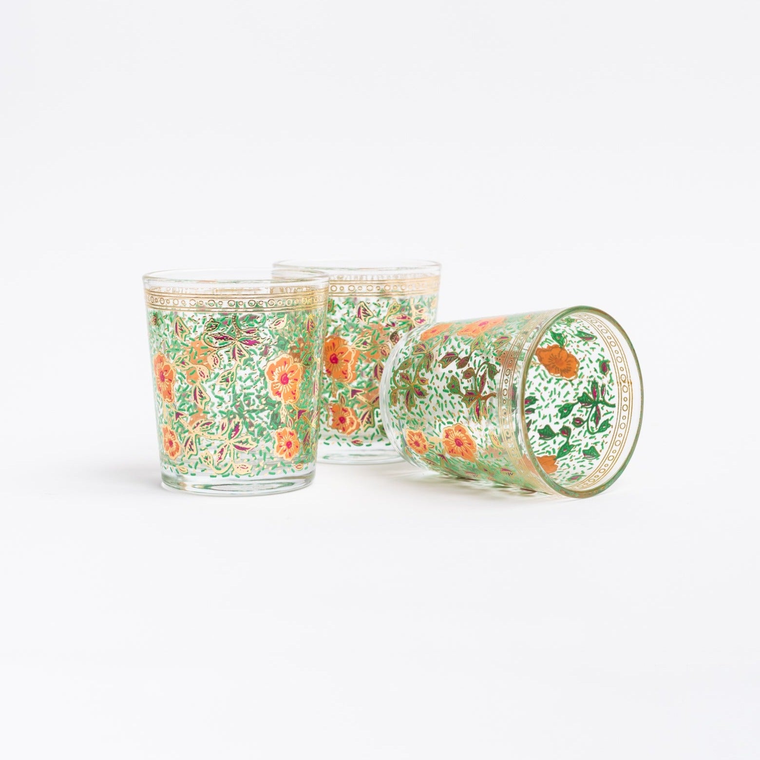 Drinking glass with green and organge floral pattern on a white wood surface