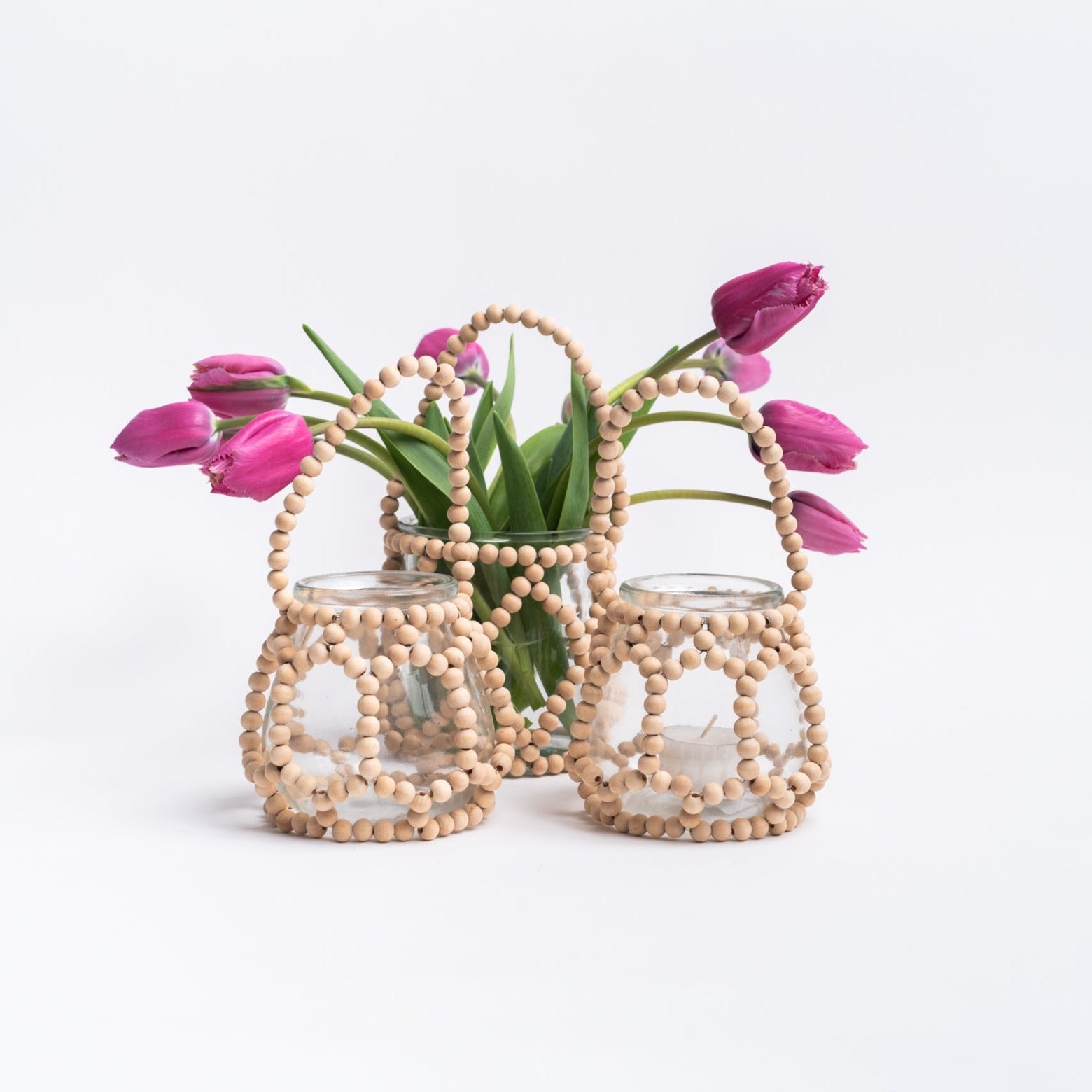 Three glass votive vases wrapped in wood beads with handles on a white background