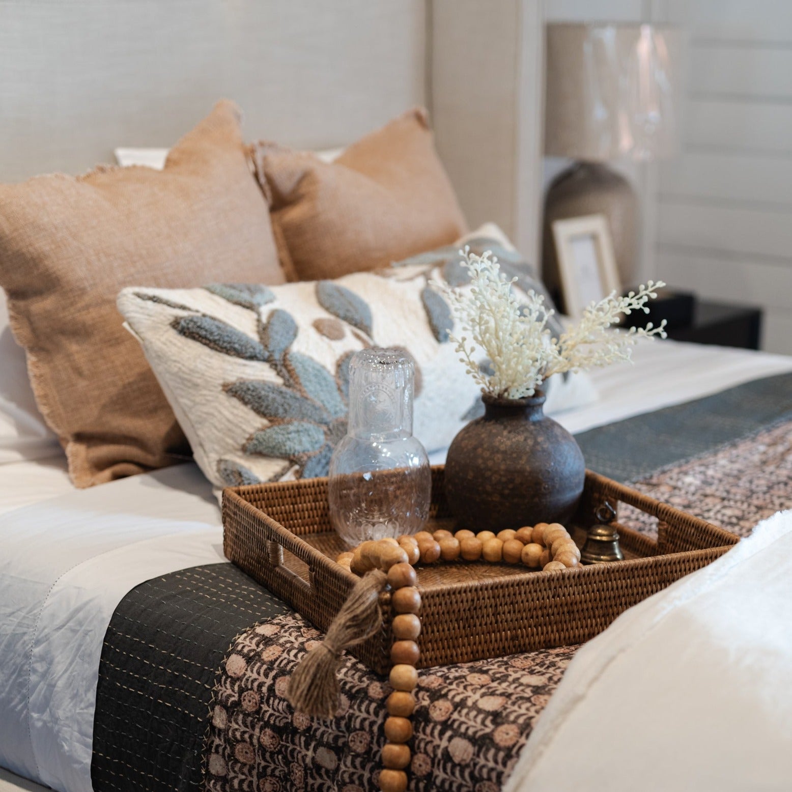 Cream colored upholstered bed with rattan tray and with beads and brown and pink and blue pillows 