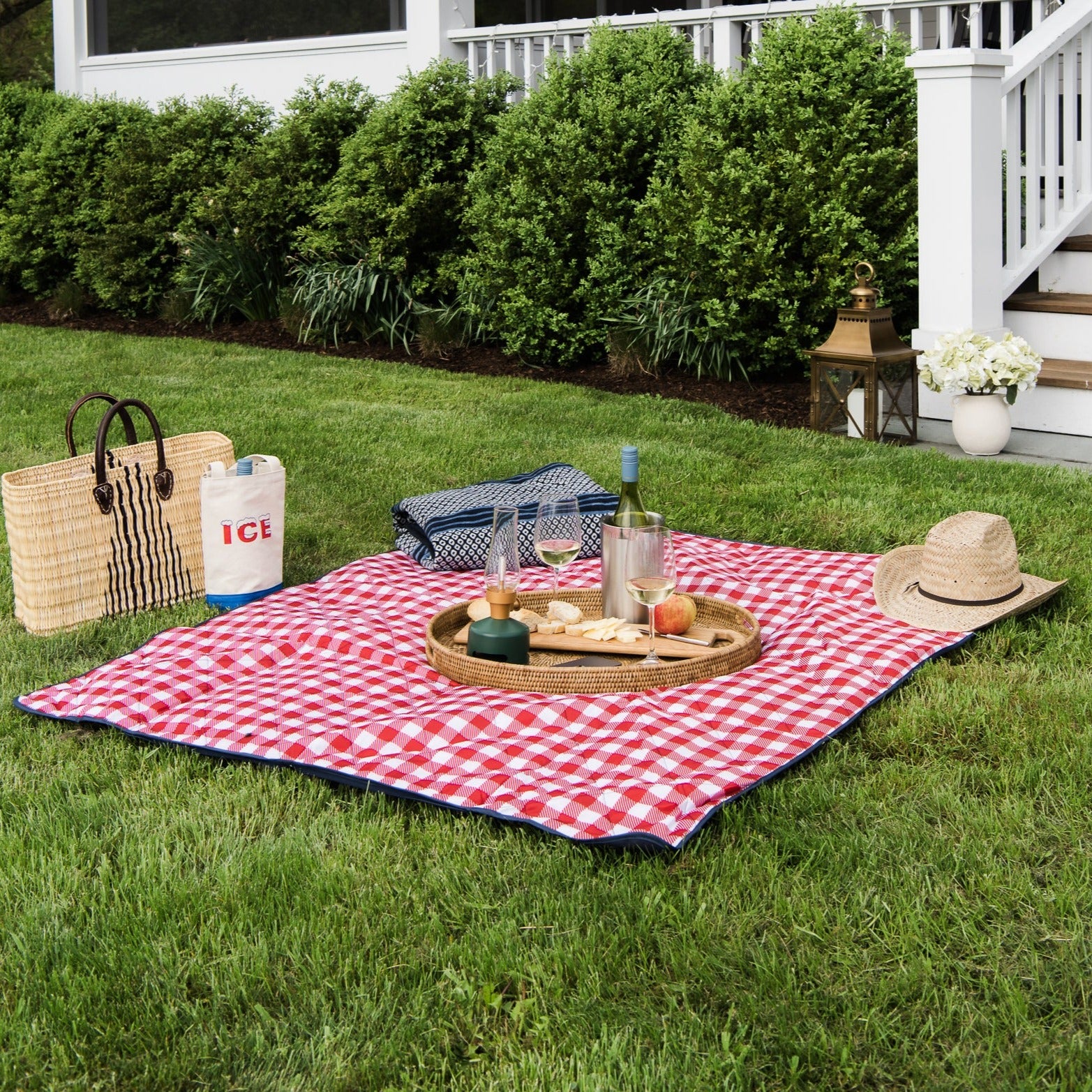 Red and White Check Outdoor Picnic Blanket with navy blue backside on a lawn in front of a house