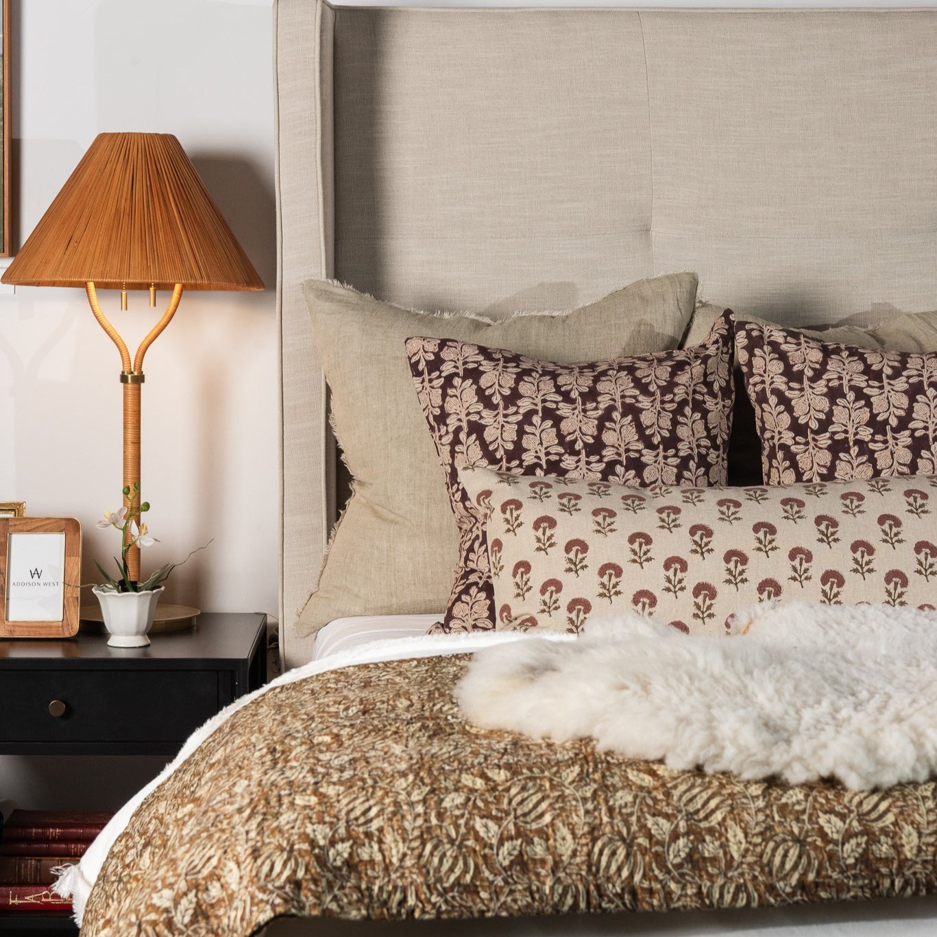 Upholstered bed with dark burgundy block print pillows and plaid throw blanket 