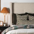 Upholstered bed with dark green block print pillows and plaid throw blanket 