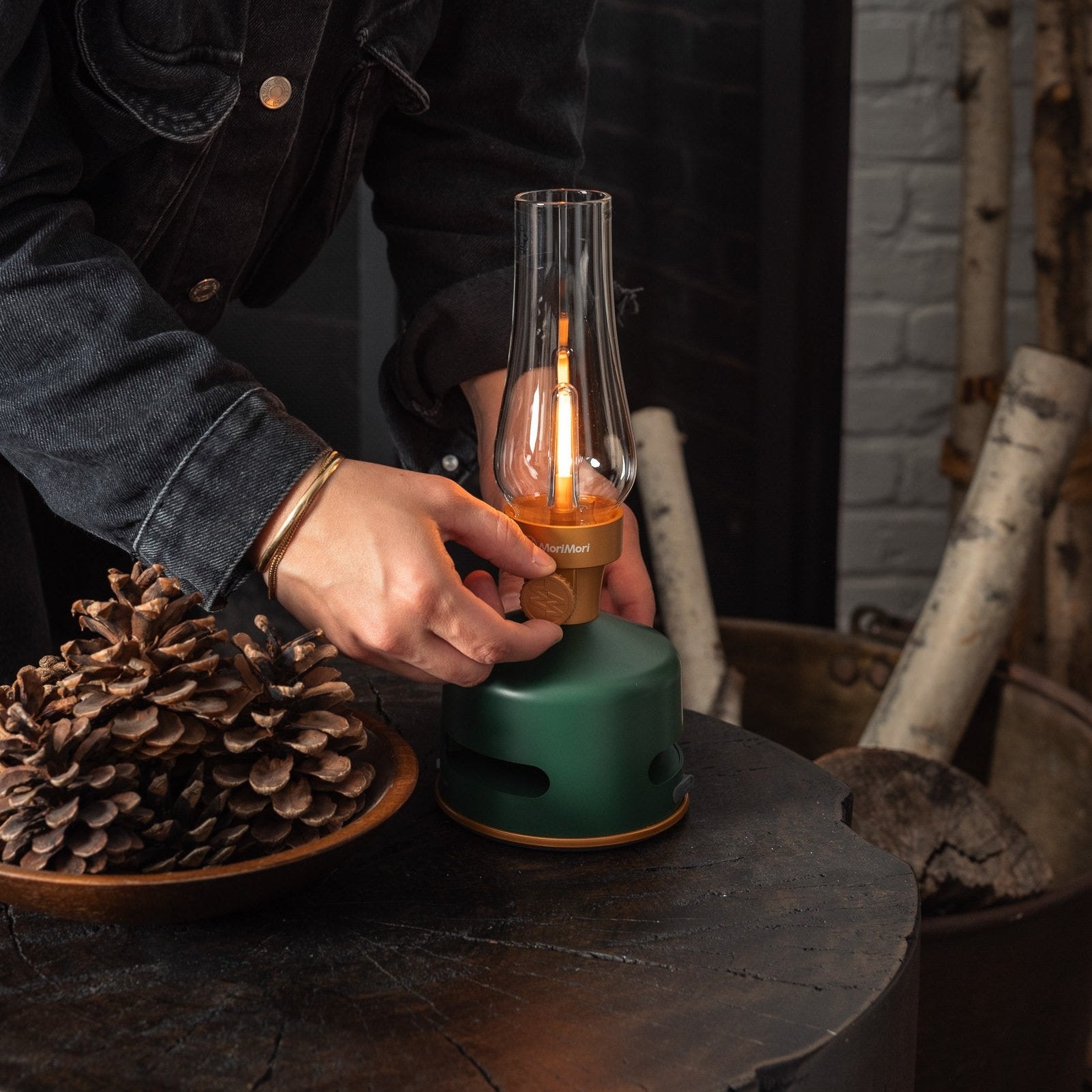 Light and Sound LED Lantern in Basil on a dark wood end table with a person adjusting the brightness dial