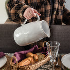 Simple Stoneware Pitcher being held by a woman at a table.