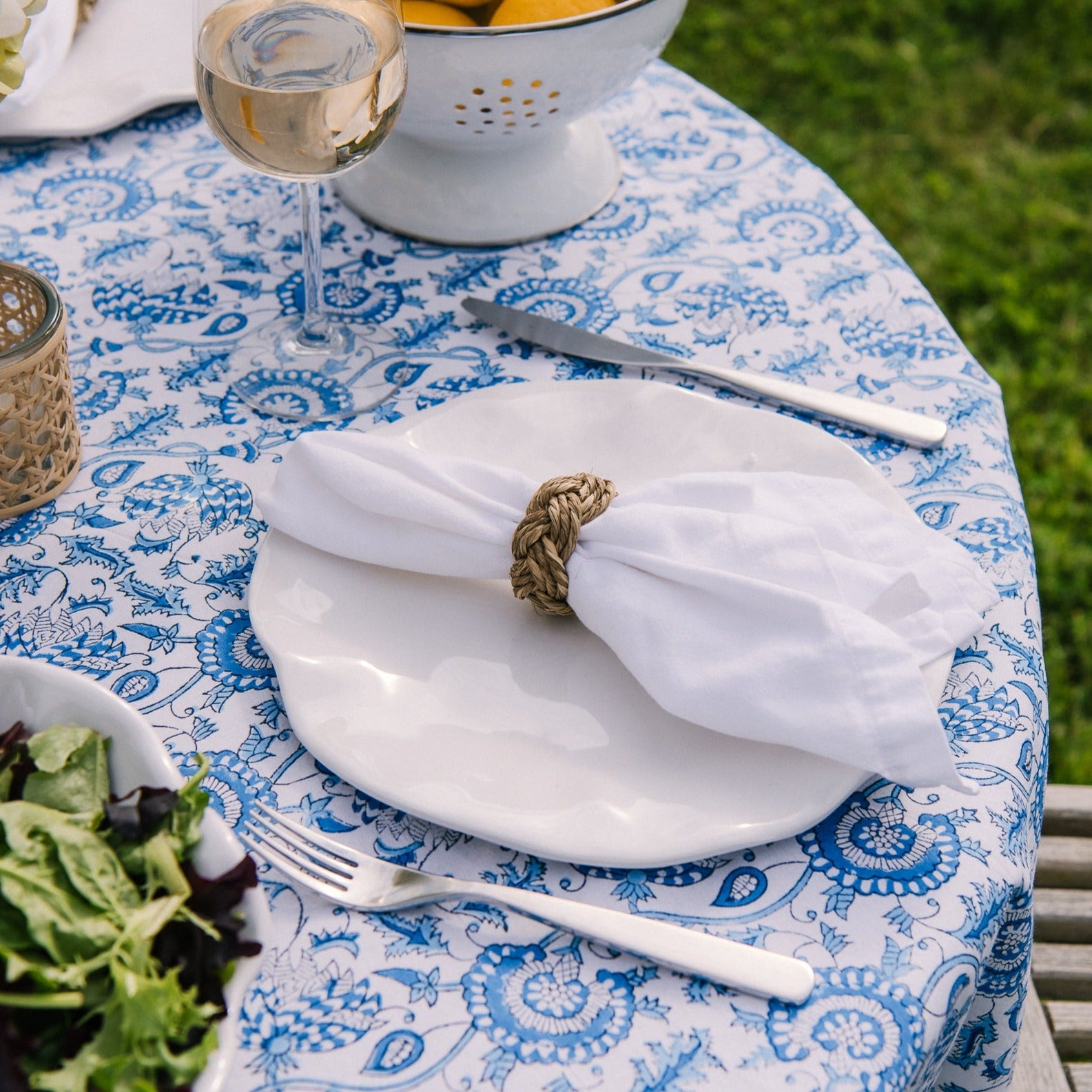 Beige linen napkin with seagrass braided napkin ring on an outdoor dining table