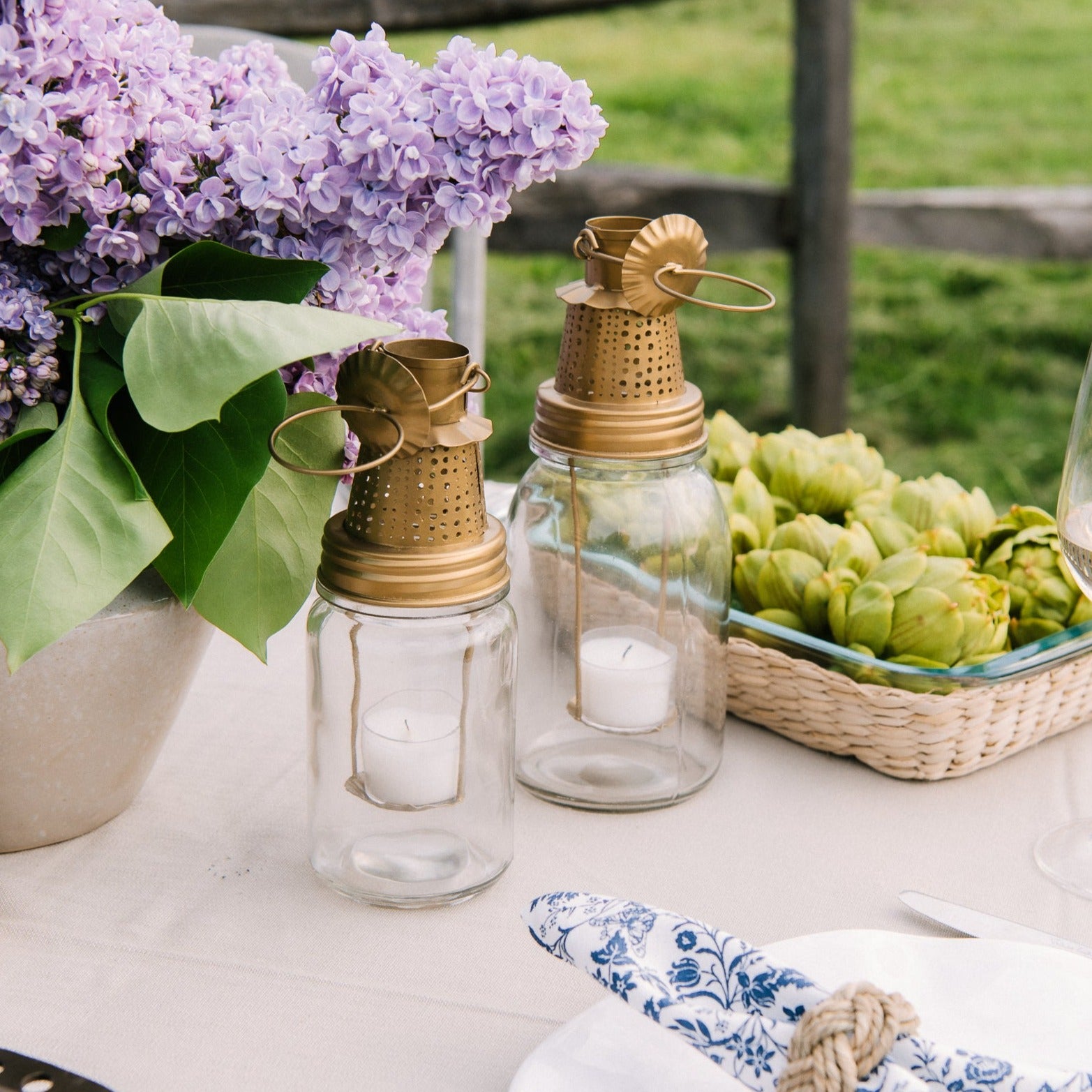 Fhia lantern in brass in two sizes on a table next to a vase of lilac flowers