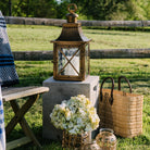 Brass lantern with crisscross glass and arched top on a concrete table in front of a fence outside