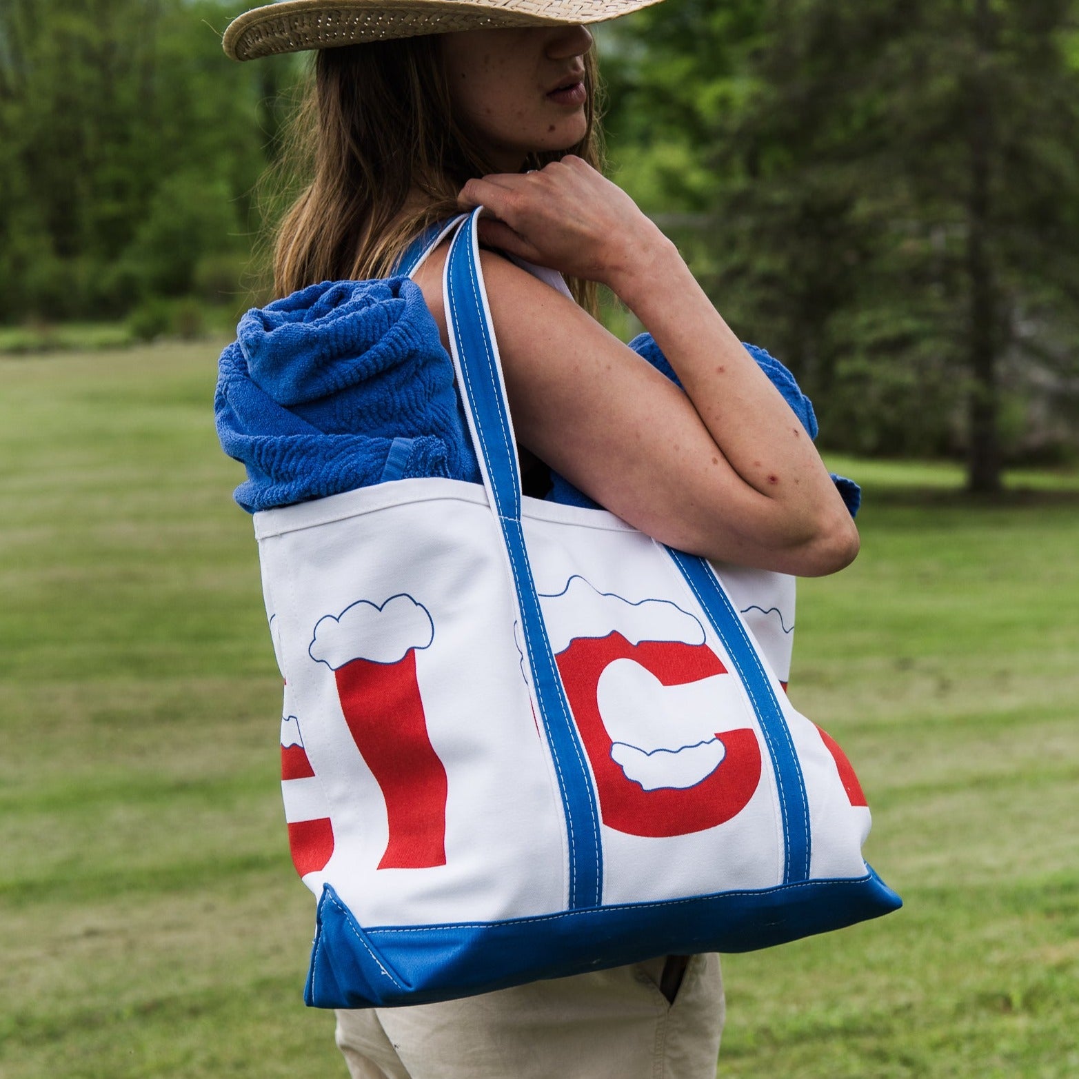 Crab and Cleek large white canvas tote bag with white royal blue bottom and straps and retro red and white ice logo being held by a woman in a blue and red stripe dress