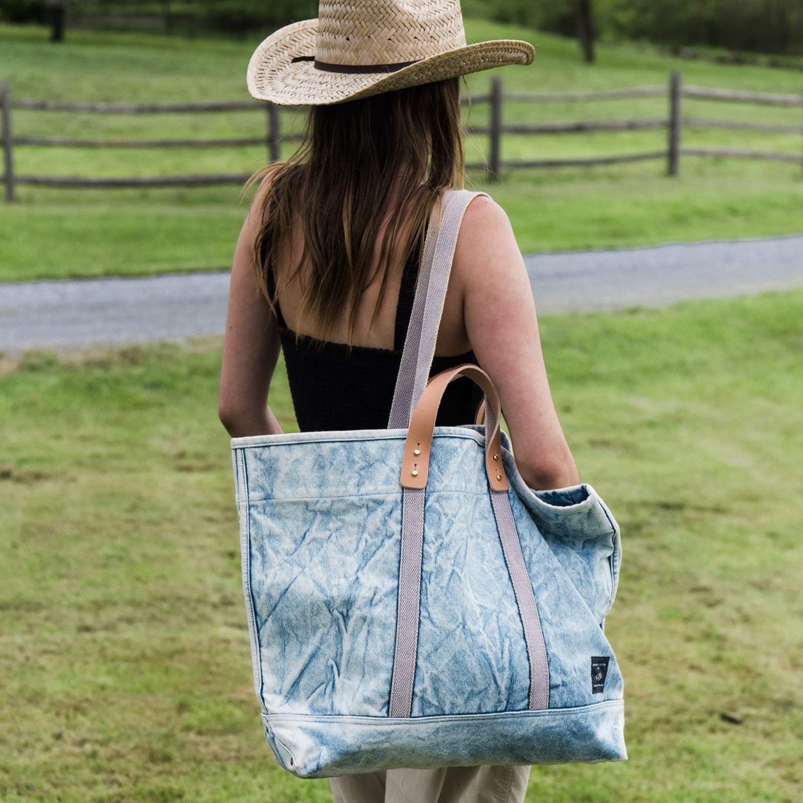 Immodest Cotton Large East-West Tote in Acid Wash on the shoulder of a woman in a green field