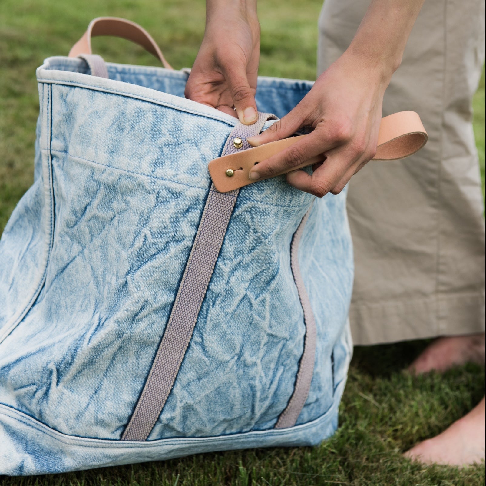 Immodest Cotton Large East-West Tote in Acid Wash with a woman taking off the removable leather handle