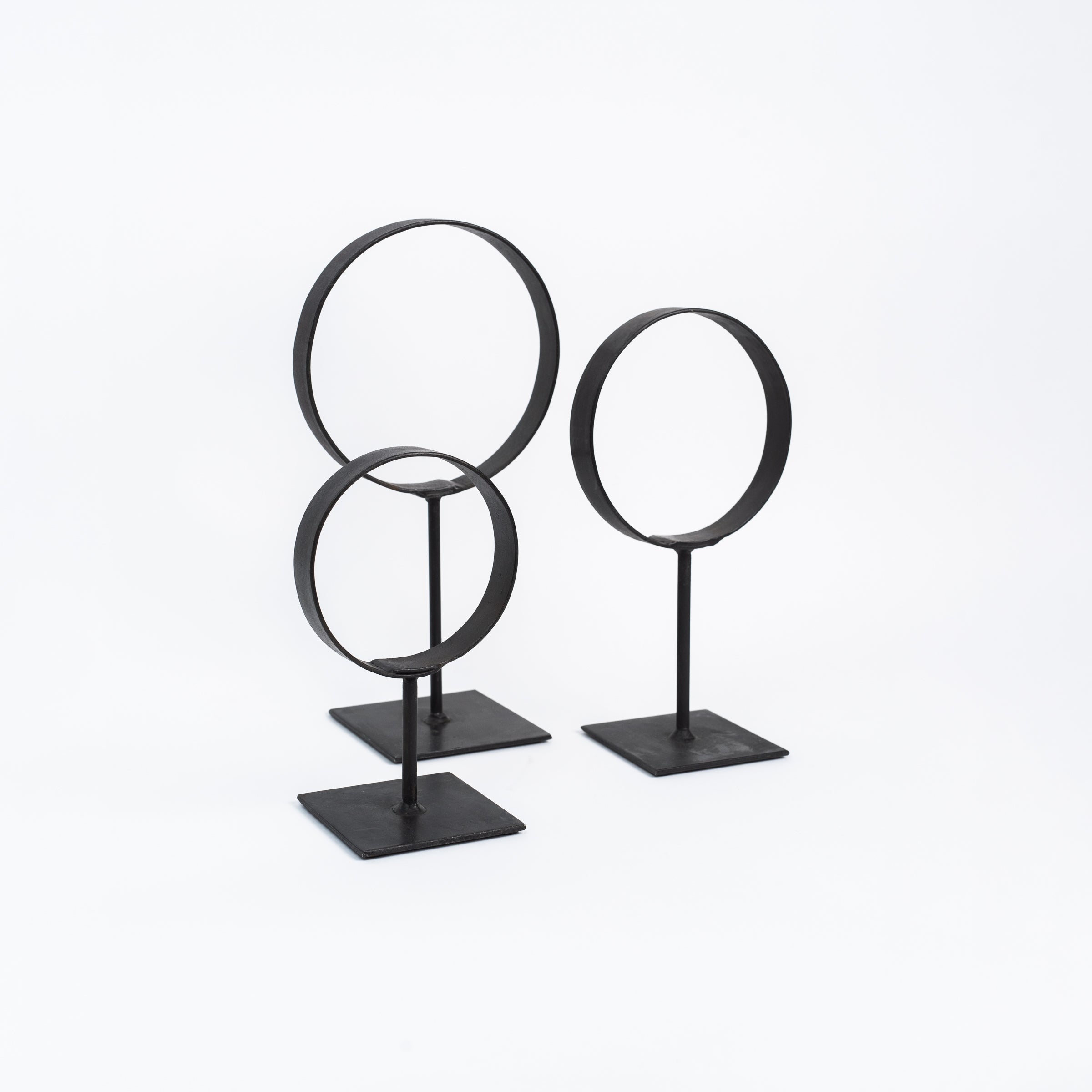 Set of three decorative black iron metal rings on stands on a white background