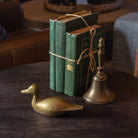 Vintage brass duck and brass bell with set of green vintage books on a dark wood table at Addison West