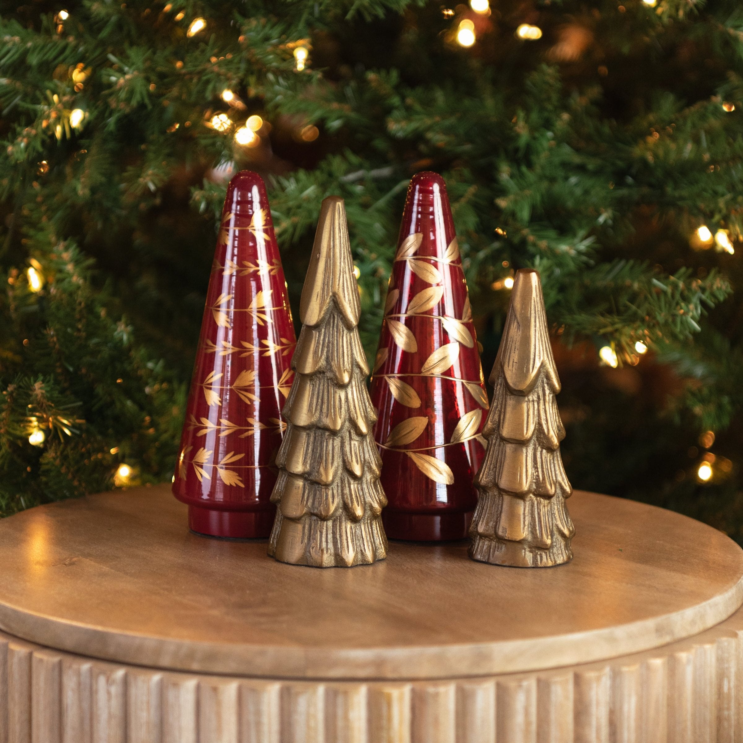 Deck The Halls Glass Tree and brass tree in front of a Christmas tree with lights at Addison West