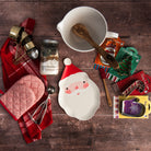 Meri Meri Santa Plate, cookie cutter cards, chocolate chip cookie mix in a mason jar, red kitchen towel, and ceramic mixing bowl with spout and handle on a wood table at Addison West.