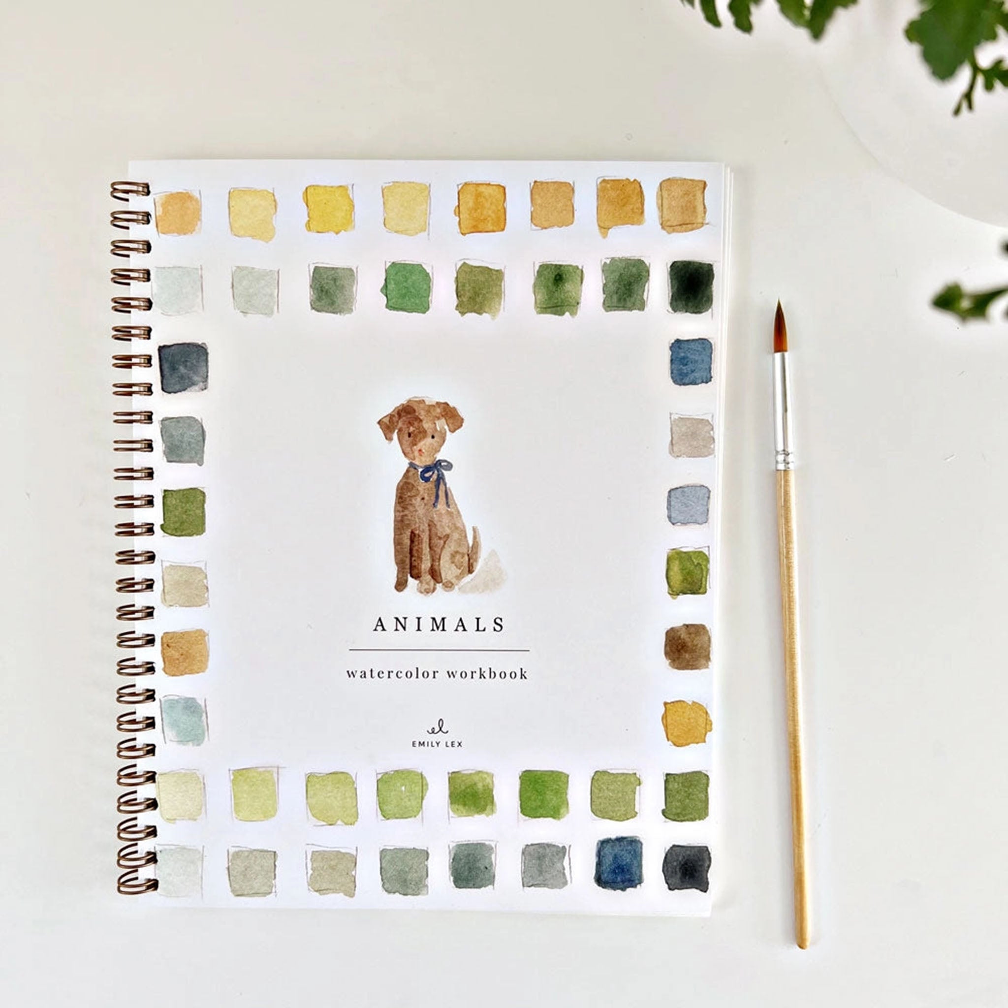 Emily lex studio Animals Watercolor Workbook on a white surface next to a paintbrush and greenery