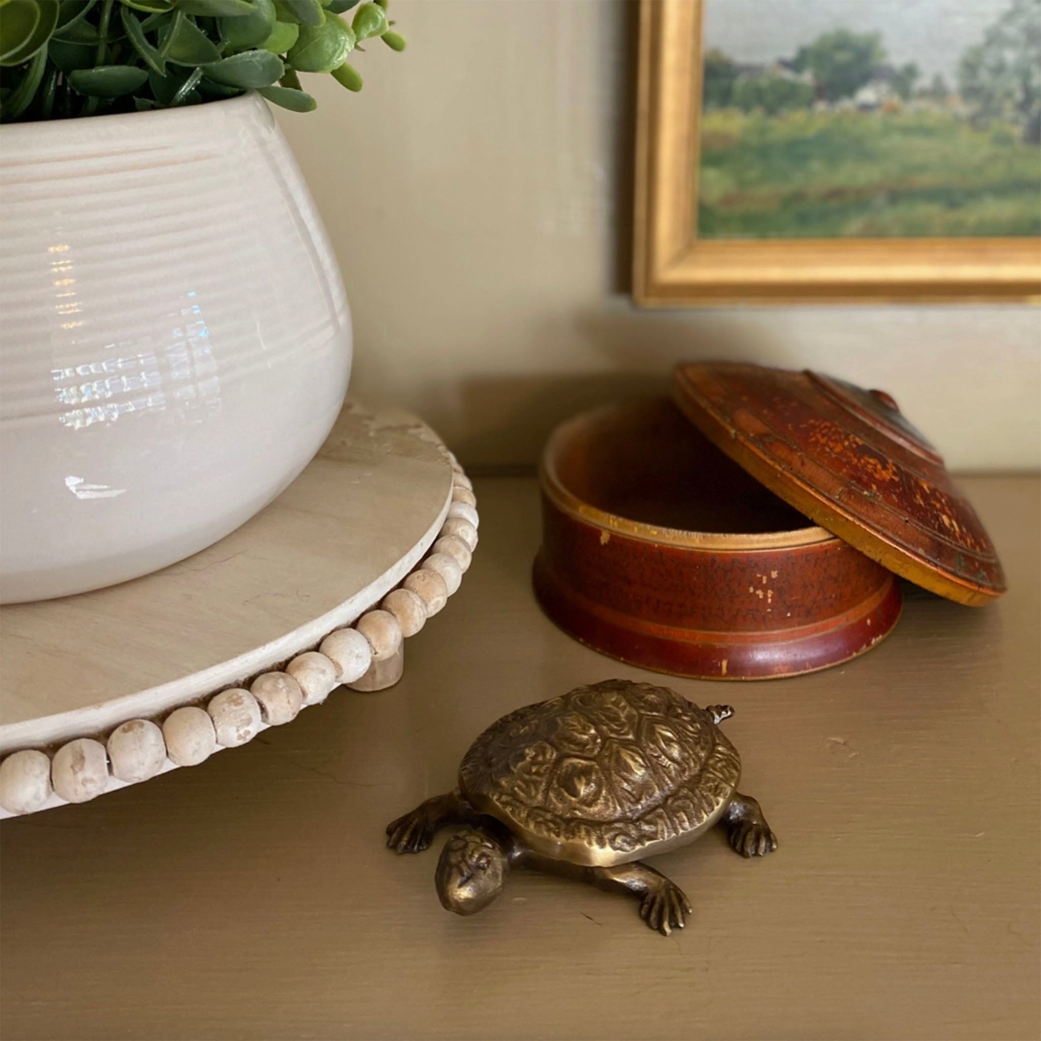 Antique brass turtle box on a shelf with other decorative items and a vintage painting in the background