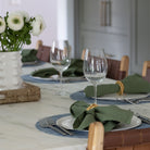 Chilewich Mini Basketweave Round Placemat in chambray blue on a table with white plates and green naplins