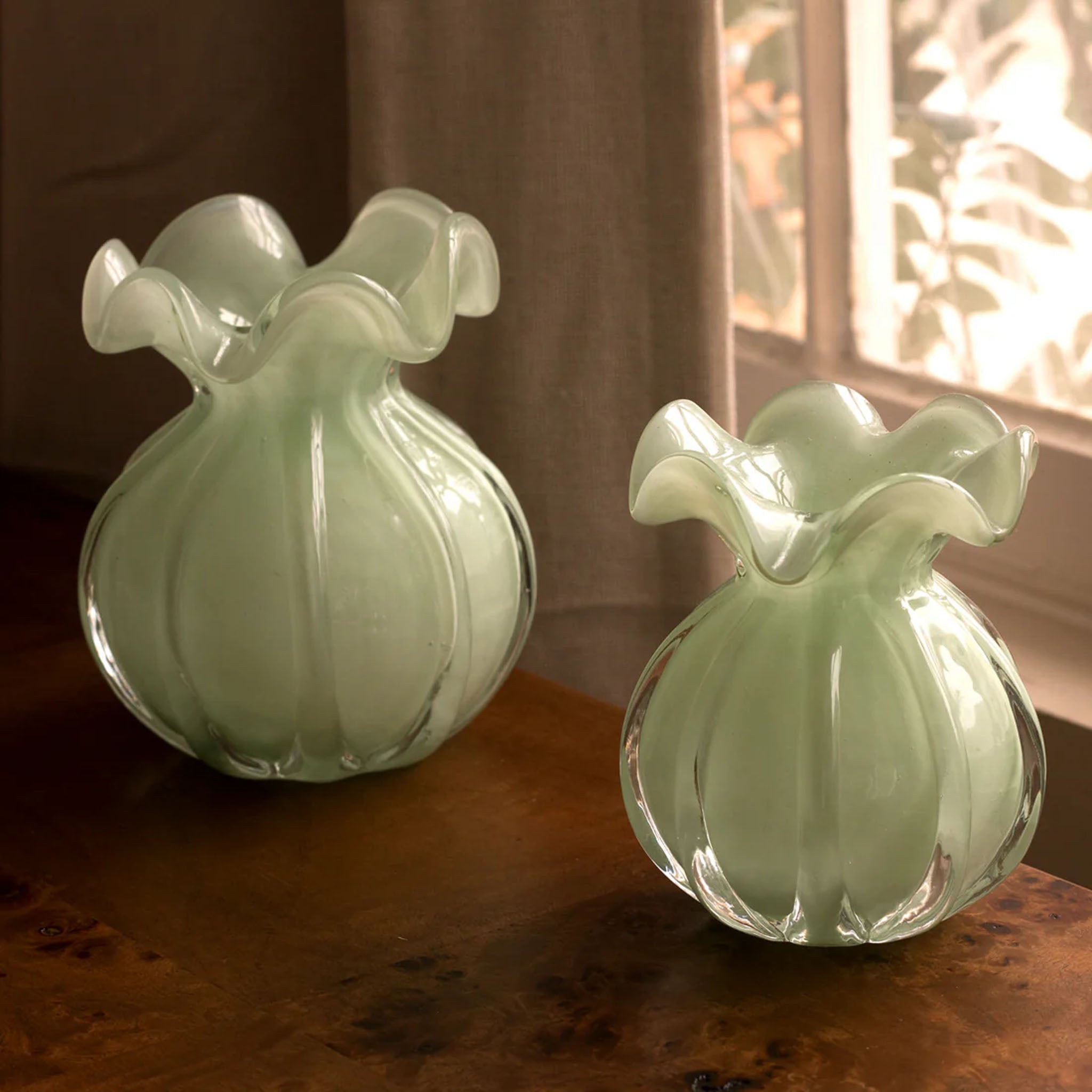 Beatriz Ball Medium Vento Bud Vase in Jade on a wood table in front of a window at Addison West