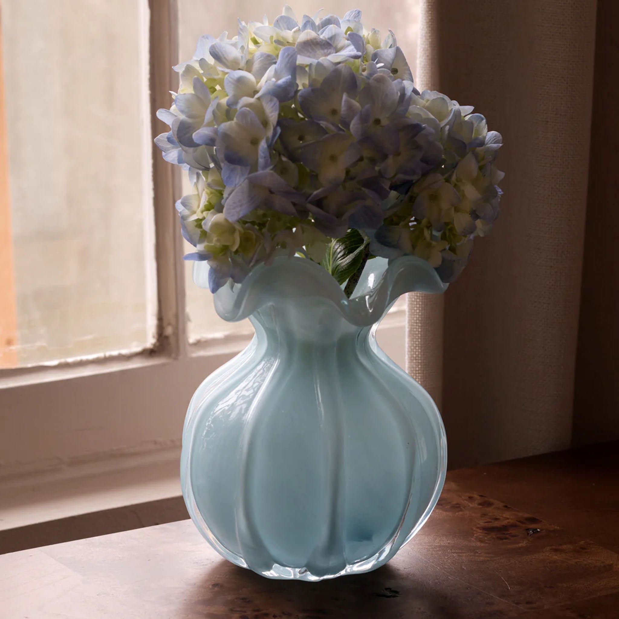 Beatriz Ball Medium Vento Bud Vase in Sky on a wood table in front of a window at Addison West