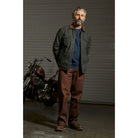 Model wearing Brixton Men's Builders Durham Jacket in Washed Black in front of a garage door and a motorcycle