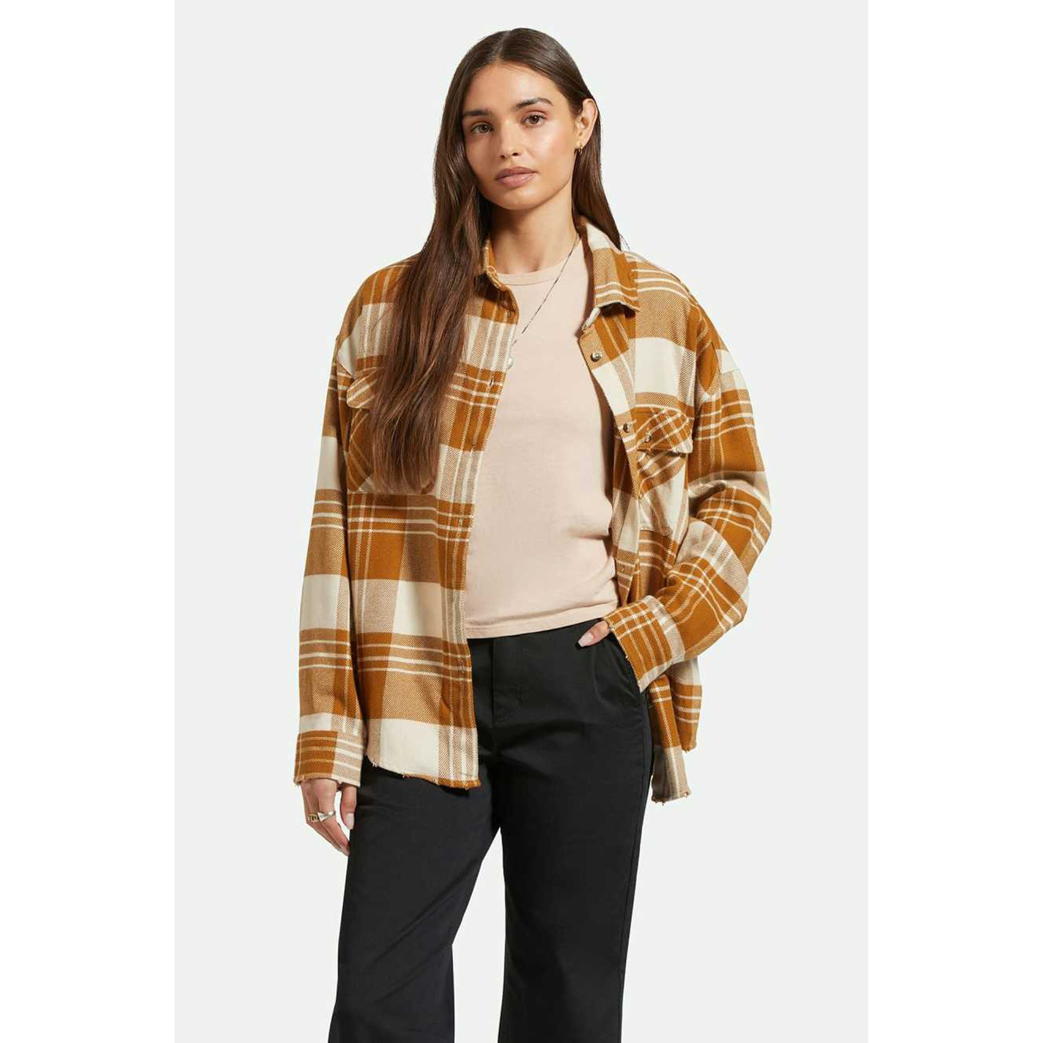 Model wearing Brixton Women's Bowery Flannel in Washed Copper Plaid with black pants in front of a white background