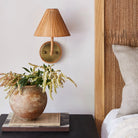 Delphine Sconce next to a nightstand with flowers and a bed