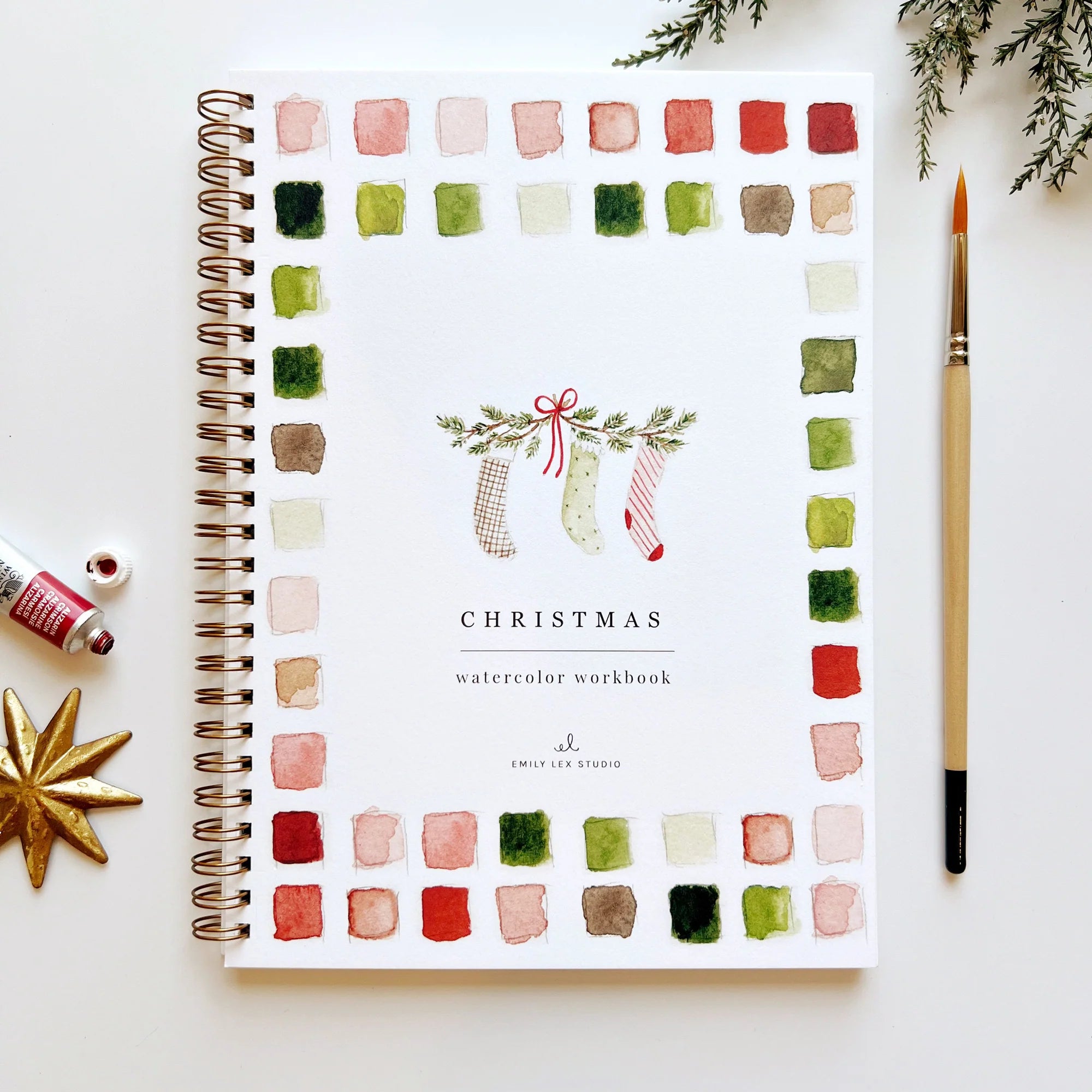 Emily Lex Christmas Watercolor Workbook on a white surface with christmas decorations and a paint brush 