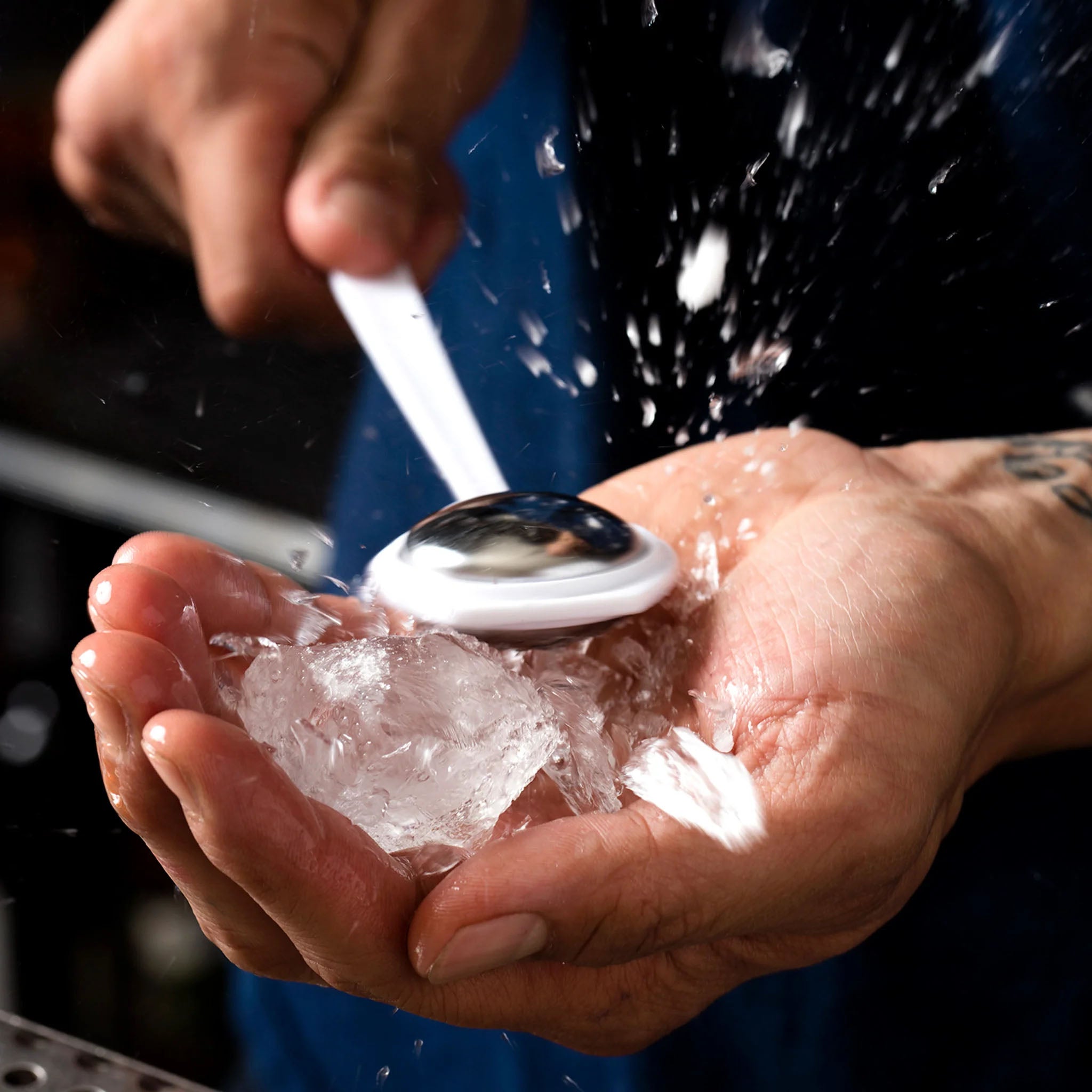 Persons hand with ice in it and the cocktail kingdom ice tapper breaking the ice