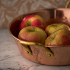 Copper pan with brass handle with apples inside on a marble counter 