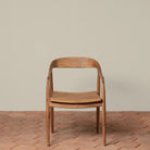 Ingrid Arm Chair in Teak against a beige background and brick floor