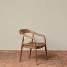 Ingrid Arm Chair in Teak against a beige background and brick floor