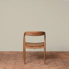 Ingrid Arm Chair in Teak against a beige background and brick floor