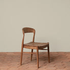 Ingrid Side Chair in Teak on a beige background and brick floor