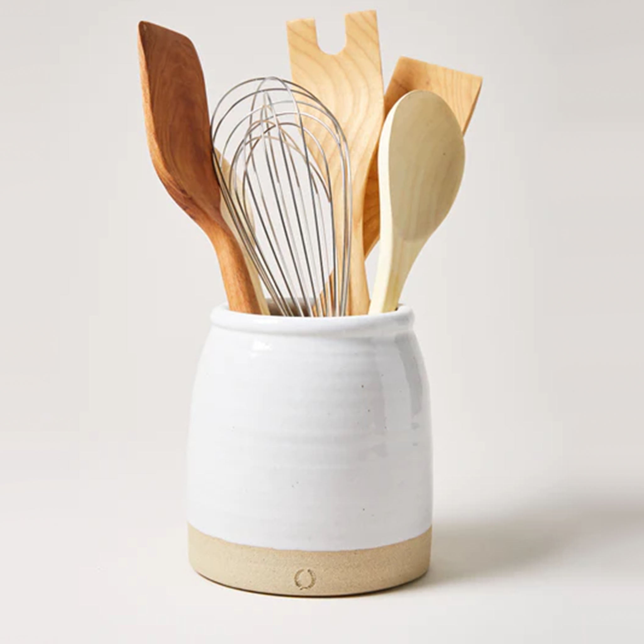 Farmhouse pottery beehive crock filled with cooking tools on a white background