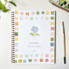 Emily lex studio Flowers Watercolor Workbook on a white surface with a paint brush and greenery