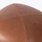 Close up of Four Hands Alma Ottoman in Brickhouse Cognac on a white background