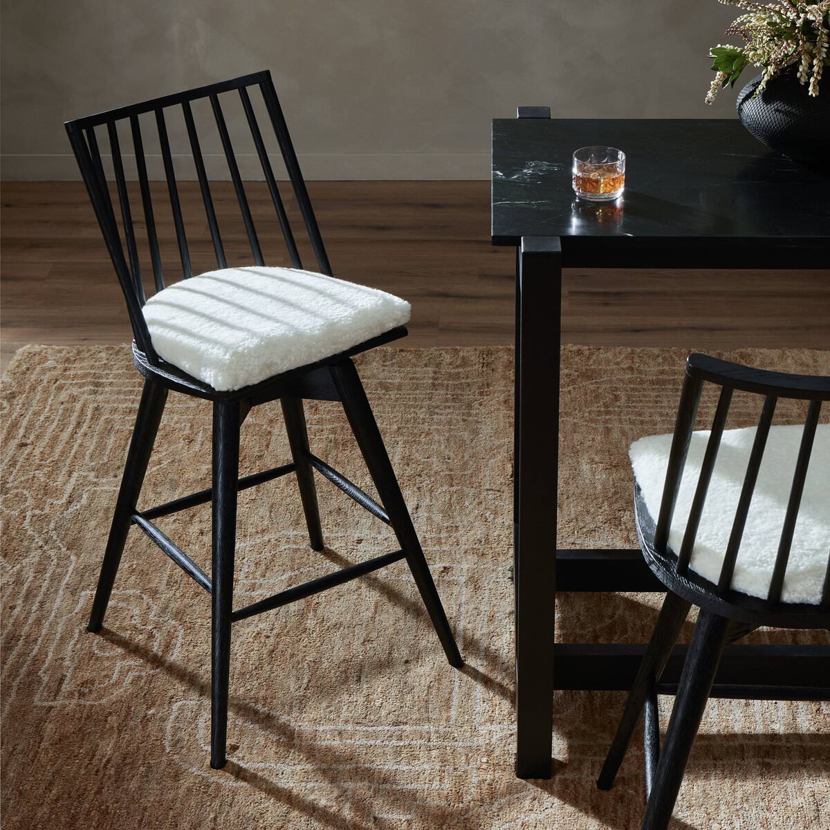 Four Hands Lewis Swivel Bar & Counter Stool in Cream Shorn Sheepskin at a black marble bar table at Addison West