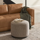 Four Hands Sinclair Round Ottoman in Barrow Taupe in a neutral living room in front of a leather couch