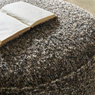 Close up of Four Hands Sinclair Round Ottoman in Ivan Granite with a book on top