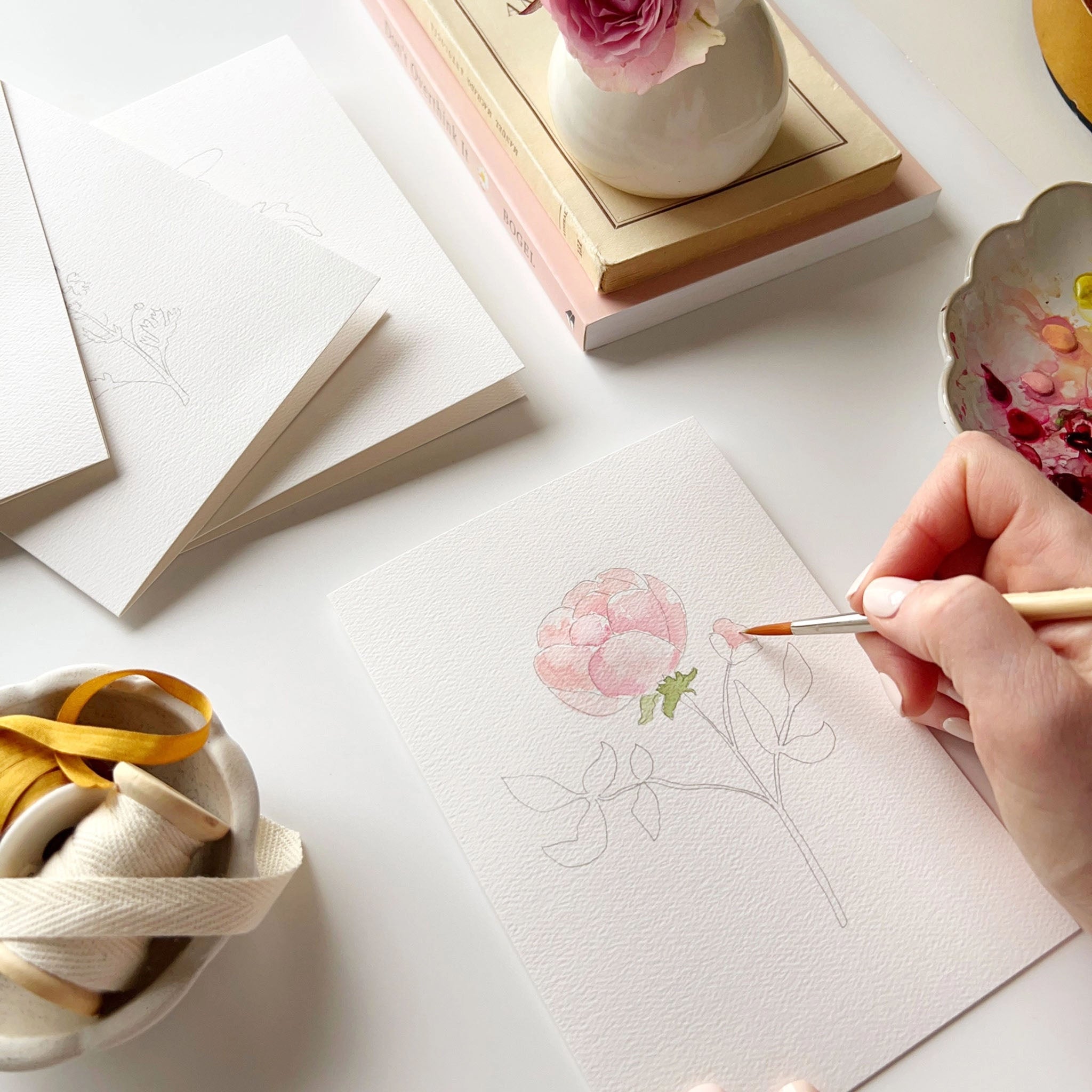 Hand painting a floral water color notecard by emily lex studio on a table with books and paint