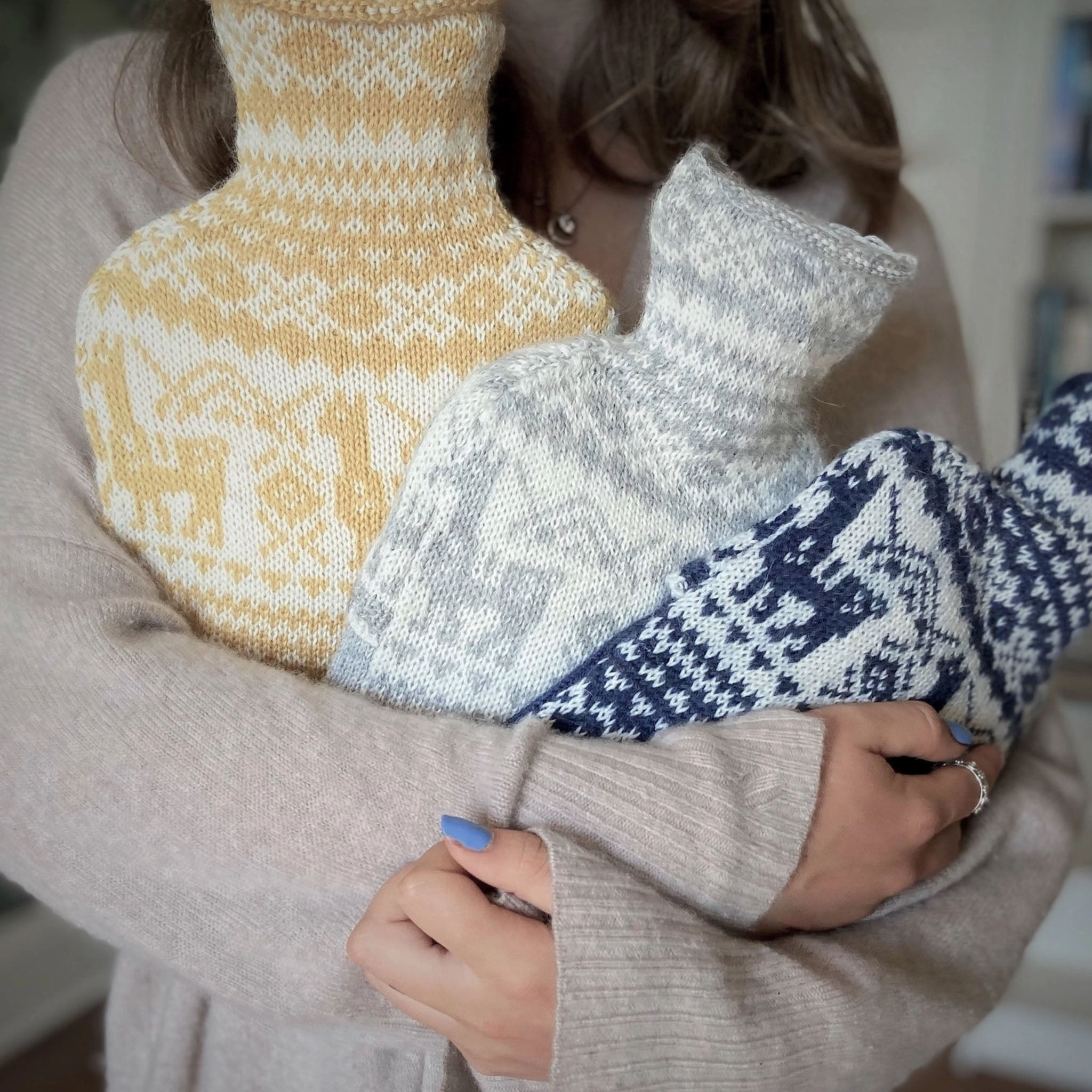 Woman holding three hot water bottles with fair isle albaca patterned covers