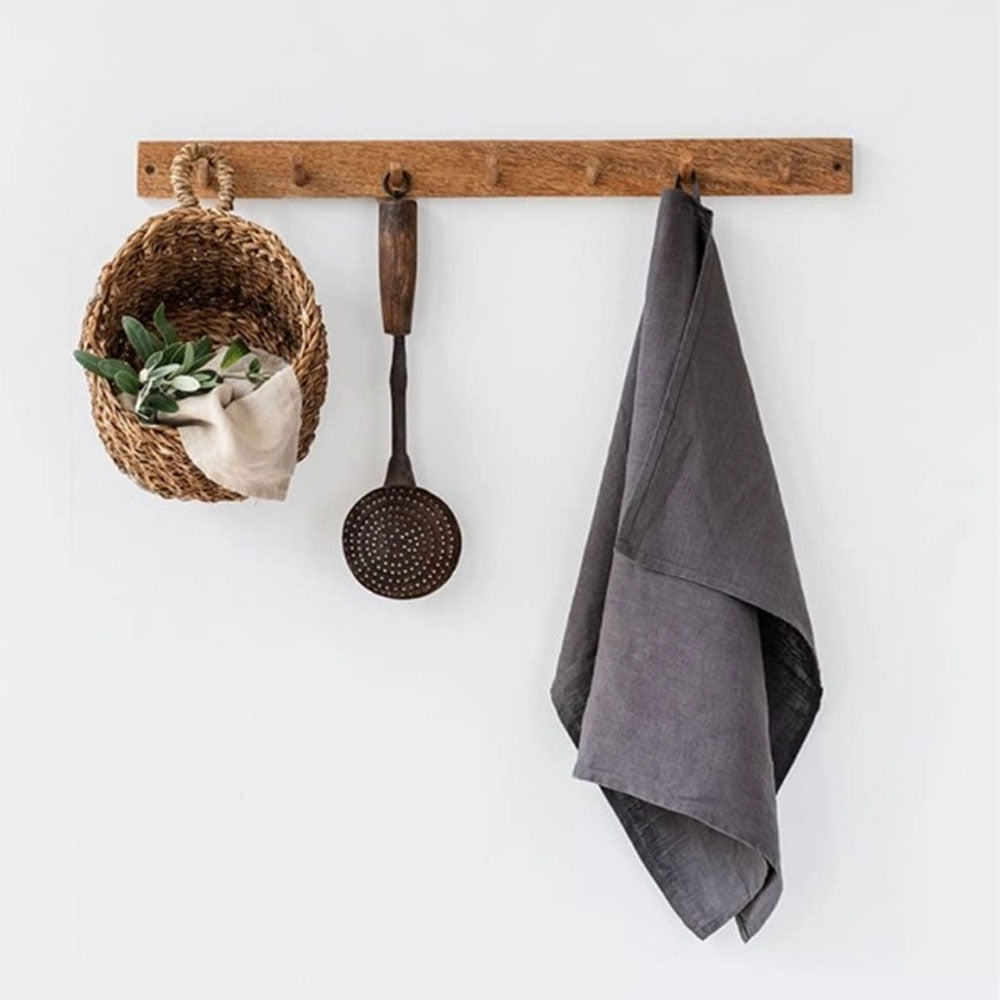 Charcoal grey linen tea towel on a wood hook next to a basket and ladle on a white background